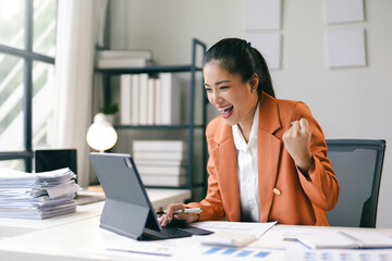 Successful businesswoman feeling happy and raising her arm with excitement while working on a...