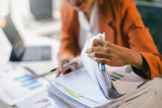 Businesswoman is searching through a stack of paperwork at her desk, looking for financial information