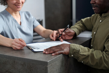Patient signing documents at medical reception desk while medical professional is assisting