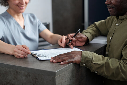 Patient signing documents at medical reception desk while medical professional is assisting