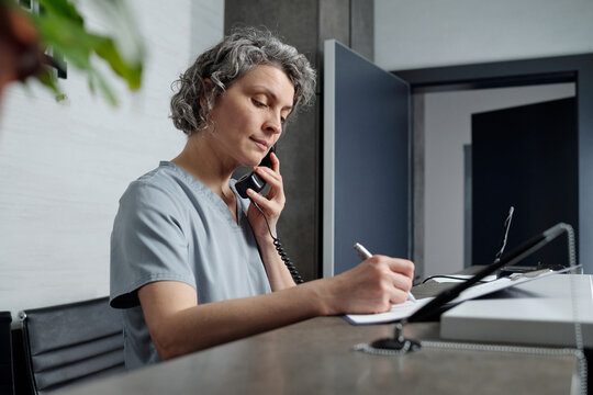 Caucasian woman working in office, jotting down notes during phone call, reflecting professionalism