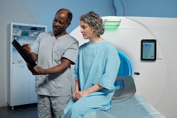 Doctor showing radiology results to senior patient sitting on examination table, engaging in detailed discussion regarding medical evaluation