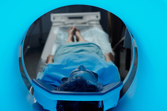 Patient lying in MRI machine for diagnostic scan, head first into tunnel, wearing medical gown for procedure