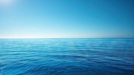 Obraz premium A vast expanse of blue water under a clear blue sky, with the warm rays of the sun shining down