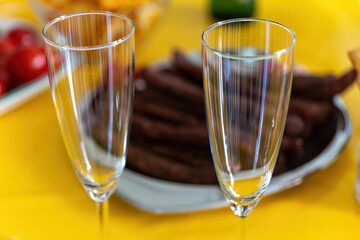 two champagne flutes sit on a yellow table next to a plate of food