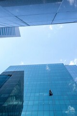Worker cleaning mirrored windows with a reflection of the sky and clouds of a commercial building in S&atilde;o Paulo, Brazil.