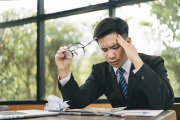 Asian Businessman being depressed by working on the laptop computer in office.Strain,Young business man to think and not Work with stress Pretending to put his hand to the head