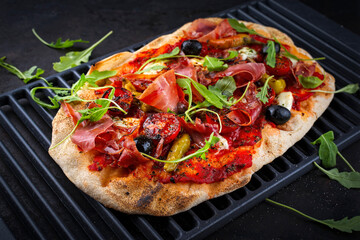 Traditional Italian pinsa bread prosciutto e salsa di pomodoro with Parma ham, buffalo mozzarella tomato sauce served as close-up on an old rustic grill grid