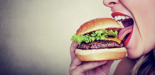 A woman with bright red lipstick preparing to bite into a cheeseburger.