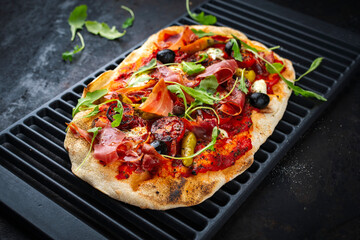 Traditional Italian pinsa bread prosciutto e salsa di pomodoro with Parma ham, buffalo mozzarella tomato sauce served as close-up on an old rustic grill grid