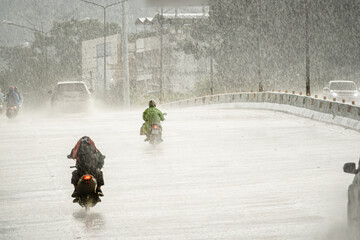 A group of motorcyclists ride down a wet road in the rain. The scene is dark and moody, with the rain creating a sense of danger and uncertainty