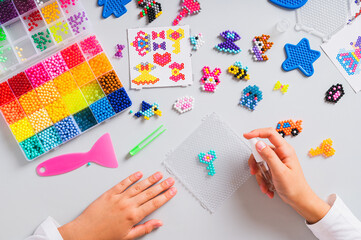 Children's hands splashing water on a thing made of aqua beads top view