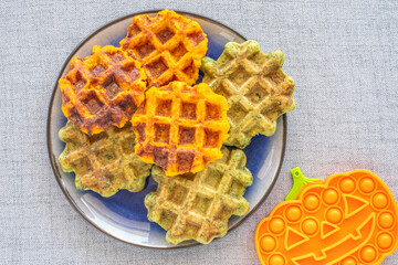 Orange and green waffles on purple plate for Halloween kid's breakfast. Pumpkin waffles and chard...