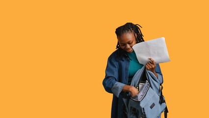 Portrait of happy woman searching through backpack, looking for school materials, studio background. Jolly girl taking out university supplies out of rucksack, preparing for college, camera B