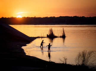 Sunset near our campsite Two boys are playing with each other in the water. Sunset in the distance. 