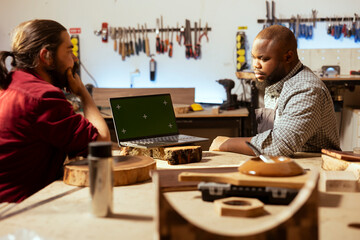 Manufacturers using CAD software on green screen laptop, debating wood design to use. Carpenters in...