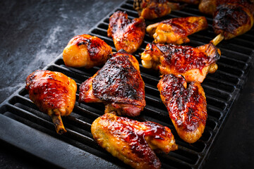 Traditional barbecue chicken wings, drumsticks and chicken breast with hot chili sauce served as close-up on a rustic grill grate