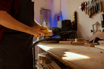 Manufacturer at workbench using manual sandpaper to sander lumber block, assembling furniture in studio. Carpenter smoothing piece of wood, sawdust flying in sunlight, close up shot