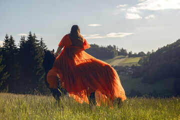 Romantic summer sundown scenery of a female equestrian wearing a dress and riding on her horse in...