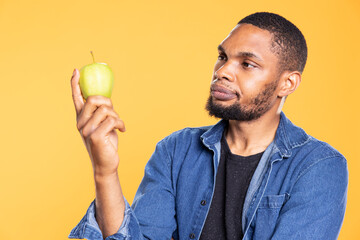 African american zero waste enthusiast looks at green apple on camera, enjoying raw healthy nutrition with ethically sourced fresh fruits. Advertising additives free eco friendly produce.