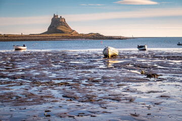 Boats during low tide on Holy island with Lindisfarne castle in the background