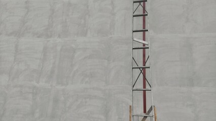 A metal ladder leans against an unfinished, unpainted wall, symbolizing ongoing construction work and the progress yet to be made