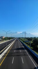 Aerial view of a highway in Sidoarjo, East Java, with Mount Penanggungan, Semeru, and Bromo in the background under a clear blue sky