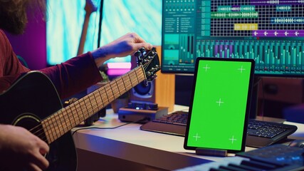 Musical producer learning to tune his guitar before playing, watching lesson tutorial video by...
