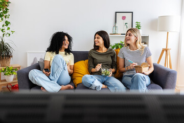 Three happy college female students working together on laptop at home. Millennial student flatmate...