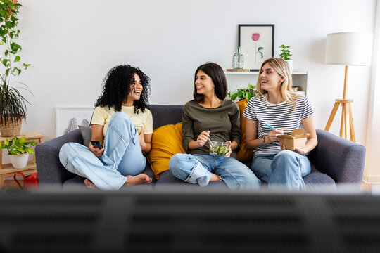 Three happy college female students working together on laptop at home. Millennial student flatmate friends enjoying time together at shared apartment.