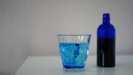 image showing a bottle filled with methylene blue  near a glass with water and methylene blue.