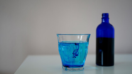 image showing a bottle filled with methylene blue  near a glass with water and methylene blue.