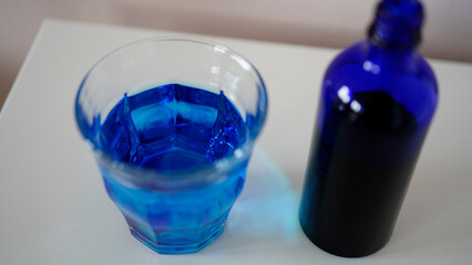 image showing a bottle filled with methylene blue  near a glass with water and methylene blue.