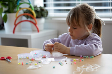 A sweet girl enthusiastically makes a bracelet of beads. A creative child engaged in jewelry making