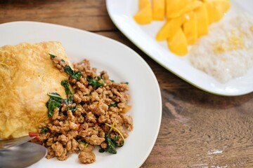 A plate of pad kra pao (holy basil pork mince stir-fry) with omelette and mixed grain rice, and fresh mango slices with sticky rice at a street food stall near the Grand Palace, Bangkok