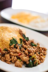 A plate of pad kra pao (holy basil pork mince stir-fry) with omelette and mixed grain rice, and fresh mango slices with sticky rice at a street food stall near the Grand Palace, Bangkok