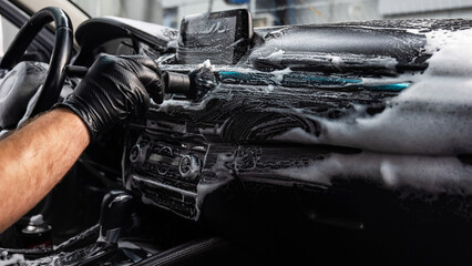 A mechanic cleans the interior of a car with a brush and foam.