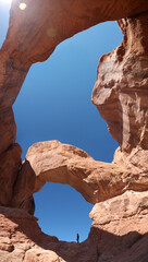 Fototapeta premium Standing under the Double Arch red rock formation, looking up to clear blue sky, Arches National Park, Utah