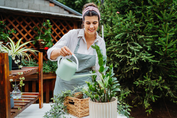 Young woman taking care of plants with water can and mister in garden

