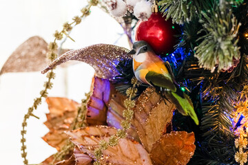 Ave decorativa navideña colorida en rama nevada con moño, hojas doradas, bolas y luces de Navidad