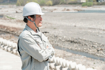 土木業・河川工事・建設現場に立つヘルメットを被った作業着姿のアジア人男性作業員
