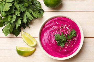 Tasty beetroot hummus, parsley and lime in bowl on light wooden table, flat lay
