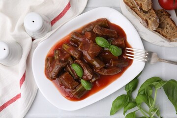Tasty stew with okra, tomato sauce, bread and basil on white tiled table, flat lay