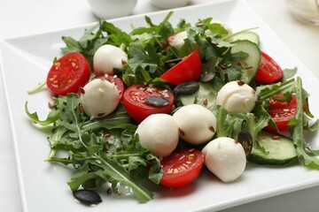 Tasty salad with arugula, mozzarella cheese and vegetables on white table, closeup
