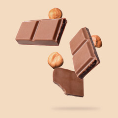 Pieces of tasty chocolate and hazelnuts falling on dark beige background