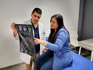 Male doctor specialist neurologist shows brain skull tomography to brunette Latin woman patient in...