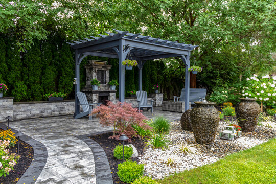 Large gray pergola on pavers with stone fireplace and waterfall urns for backyard oasis landscape design - Powered by Adobe