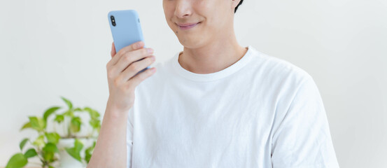 リビングで笑顔の携帯を見る私服の男性 © ponta1414