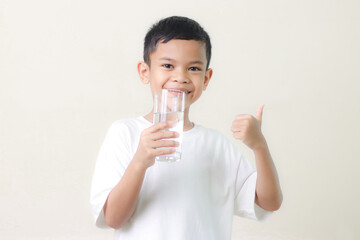 cute little asian boy Standing and Smiling little with a holding an empty glass of water on white background.