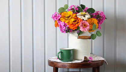rural composition with a bouquet of zinnias and phlox in a can in a white clapboard cottage....